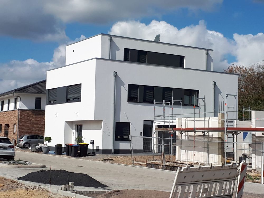 Weißer kubischer Neubau eines Einfamilienhauses während der Bauphase, angeschlossen an ein Wärmenetz